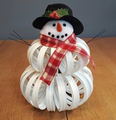 a snowman made out of white plastic tubes on a wooden table with a red scarf around it