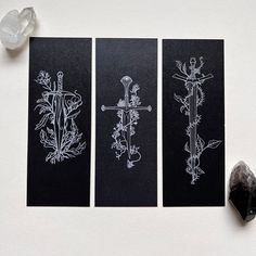 three black cards with white designs on them next to a rock and some crystal stones