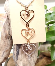 a necklace with three hearts hanging from it's side on a stand next to a plant