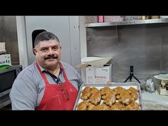 a man in an apron holding a tray of doughnuts