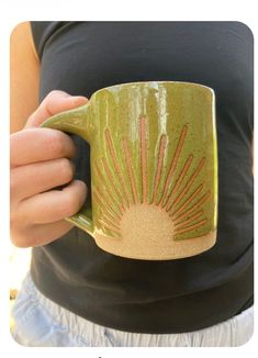 a person holding a coffee mug with the sun painted on it's front and side