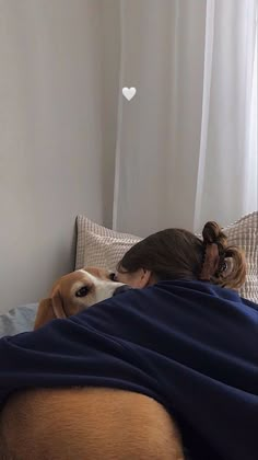 a woman laying in bed next to a dog with a blanket on it's back