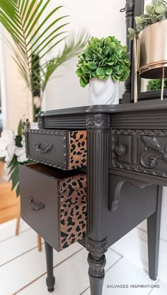 a black dresser with leopard print drawers and plants on the top, in front of a mirror