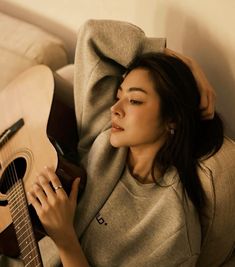 a woman laying on top of a couch holding an acoustic guitar