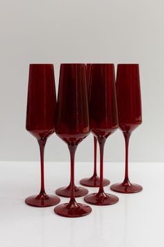 four red wine glasses sitting next to each other on top of a white countertop