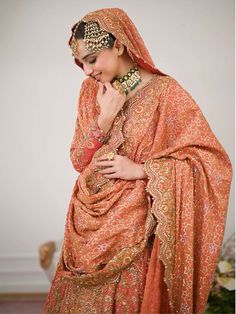 a woman in an orange dress and headpiece is standing with her hands on her chin