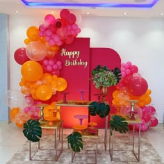 a birthday party with balloons and plants on the table in front of a pink wall