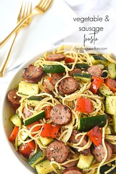 a white bowl filled with pasta, sausage and veggies next to golden forks