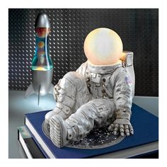 an astronaut statue sitting on top of a blue book next to a glass vase with a light in it