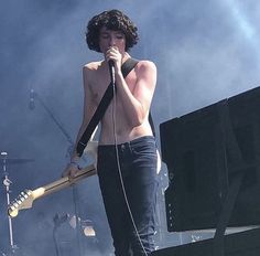 a shirtless man holding a guitar while standing in front of a microphone on stage