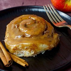 an apple cinnamon roll on a black plate with cinnamon sticks