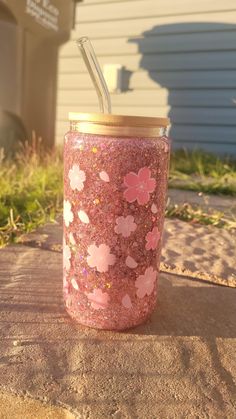 a pink glittered cup with a straw in it sitting on the ground next to a house