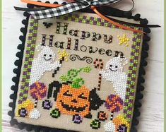 a cross stitch halloween decoration hanging on a wall next to a black and white ribbon