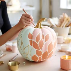 a woman is painting a pumpkin on a table with candles and other items around it