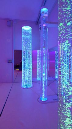 several tall glass vases are lit up with colored lights in a room filled with purple and blue lighting