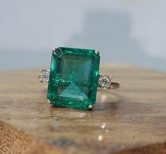 an emerald and diamond ring sitting on top of a wooden table