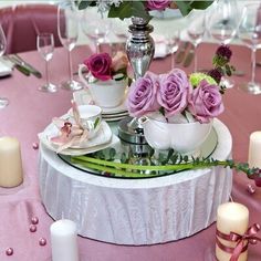 a table topped with plates and cups filled with purple flowers next to candles on top of a pink table cloth