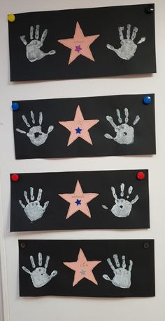 three handprints on black paper with pink and blue stars hanging from the wall