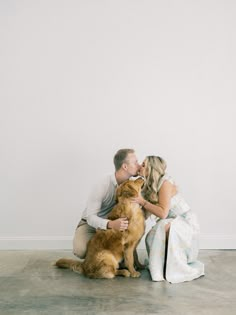 a man and woman kissing while sitting on the floor with a dog in front of them