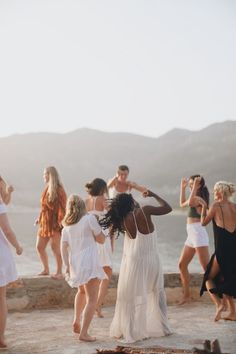 a group of women standing on top of a beach next to each other in white dresses