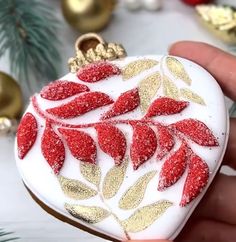 a hand holding a heart shaped ornament decorated with red and gold leaves