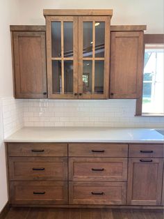 an empty kitchen with wooden cabinets and white counter tops in front of a large window