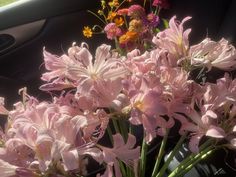 a bunch of pink flowers in a vase on the dashboard of a car with other flowers behind it