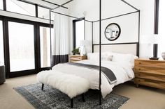 a bedroom with a four poster bed and white walls, carpeted flooring and windows