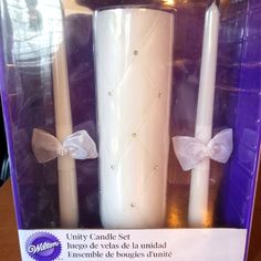 three white candles with bows on them in a purple package for sale at a store