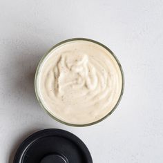 a glass bowl filled with cream sitting on top of a white table next to a black lid