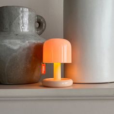 an orange table lamp sitting on top of a shelf next to a gray vase and other items