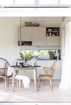 two chairs and a table in a room with white paint on the walls, an open window to the kitchen