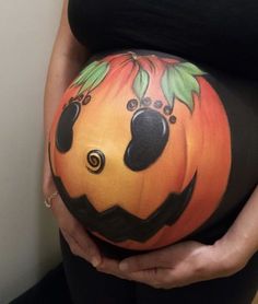 a pregnant woman holding her belly painted like a pumpkin with black and orange designs on it