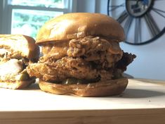 a chicken sandwich sitting on top of a wooden table next to a clock and window