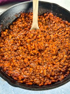 a skillet filled with baked beans and topped with a wooden spoon on the side