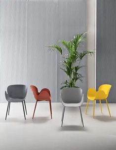 three different colored chairs sitting next to each other in front of a wall with vertical blinds