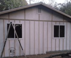 a house being constructed with siding and windows on the side of it, next to a ladder