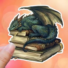 a hand holding up a sticker with a dragon on top of books