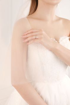 a woman in a white wedding dress with a veil on her head and wearing a diamond ring