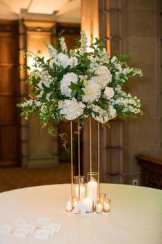 a tall vase filled with white flowers sitting on top of a table next to candles