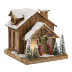 a small wooden house with snow on the roof and wreaths around the front door