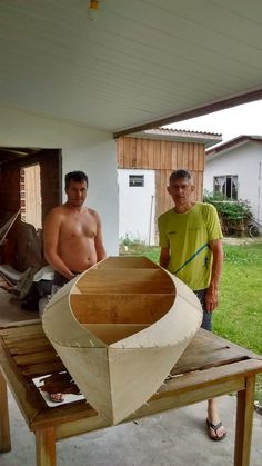 two men standing next to a wooden boat on a table in front of a house