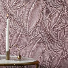 a white candle sitting on top of a table next to a wallpapered background