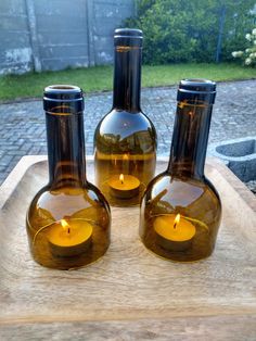 three brown glass bottles sitting on top of a wooden tray with a lit candle in them