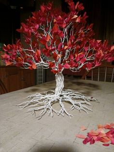 a tree that is sitting on a table with red leaves around it and roots in the middle