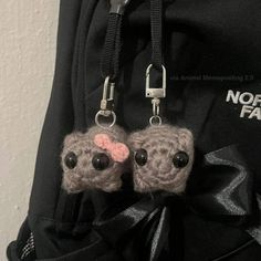 two small crocheted mice are attached to a black backpack with silver metal straps