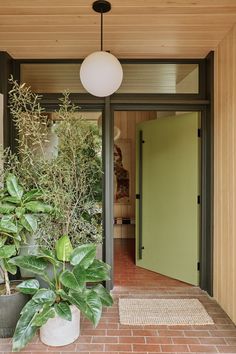 a house with green doors and plants in the entryway, next to a brick walkway