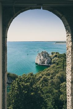 an arch in the side of a building with water and trees around it, looking out at