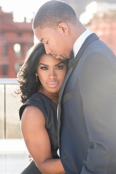 a man and woman standing next to each other in front of a building with their arms around each other