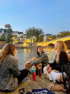 three young women sitting on the edge of a river